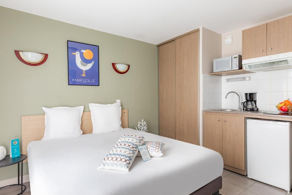 a bedroom with a large white bed and a kitchen at Appart'City Classic Marseille Euromed in Marseille