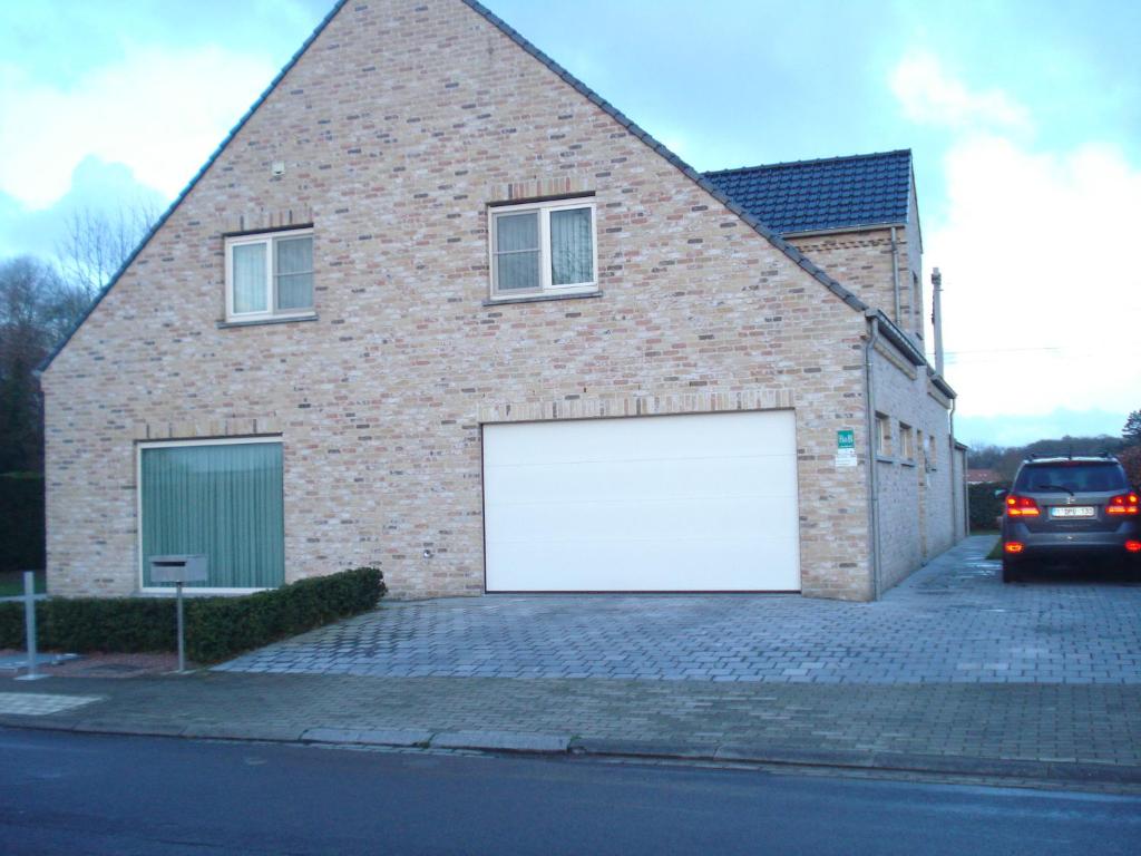 a brick building with a large white garage at Auro'ra in Zedelgem