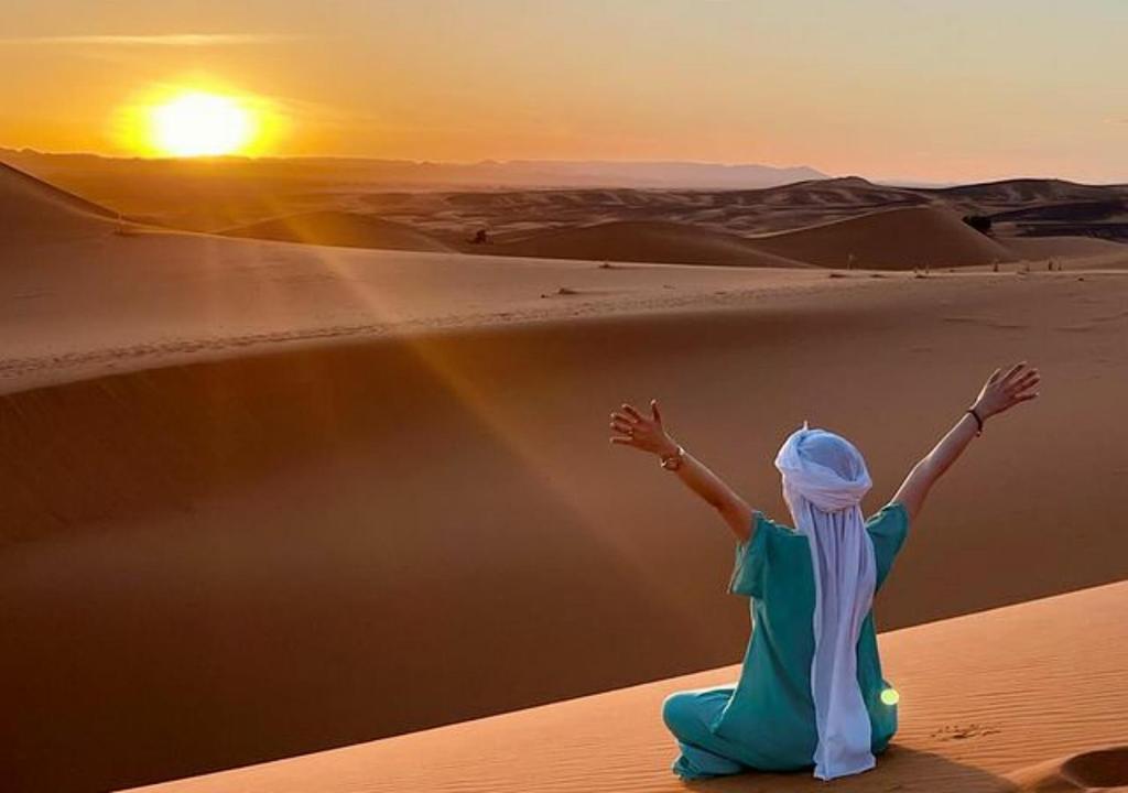 a woman sitting in the desert watching the sunset at Shiny luxury camp in Merzouga