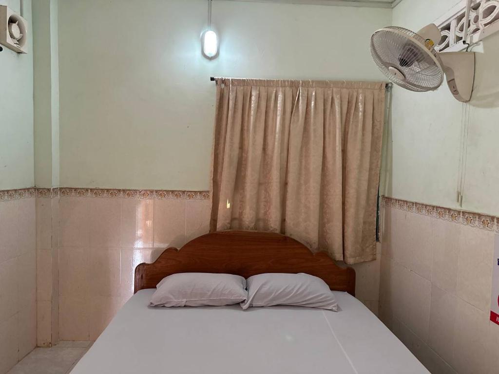 1 cama con 2 almohadas y una ventana con ventilador en Palm Tree Quest House, en Battambang