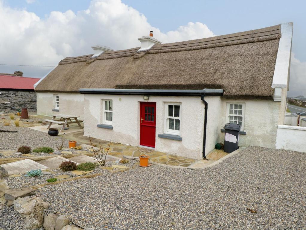 een klein wit huis met een rode deur bij Freemans Cottage in Enniscrone