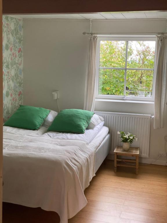 a bedroom with a bed with green pillows and a window at Camønogaarden et B&B, kursus center og refugie på Østmøn in Borre