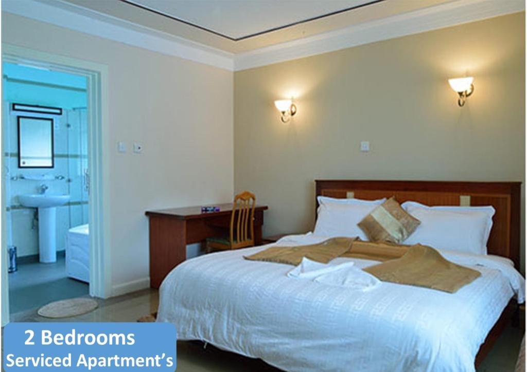 a bedroom with a large bed with a desk and a bathroom at Westland's Gardens Suites One in Nairobi