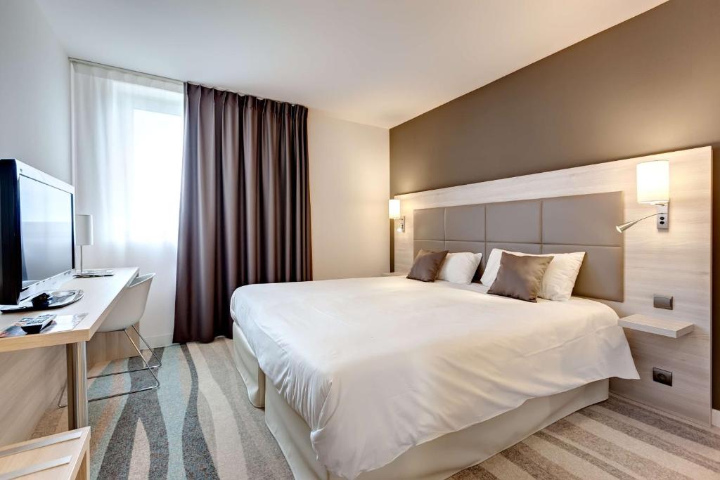 um quarto de hotel com uma grande cama branca e uma secretária em Brit Hotel Vendée Mer em La Mothe-Achard