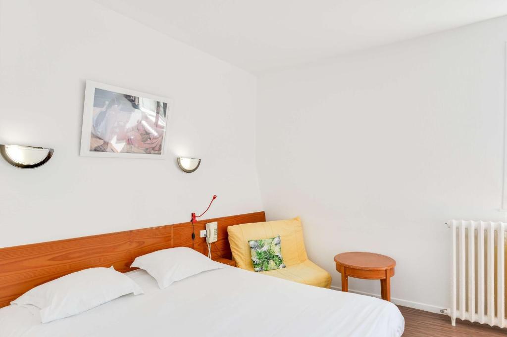 a bedroom with a white bed and a yellow chair at Brit Hotel Notre Dame in Valenciennes