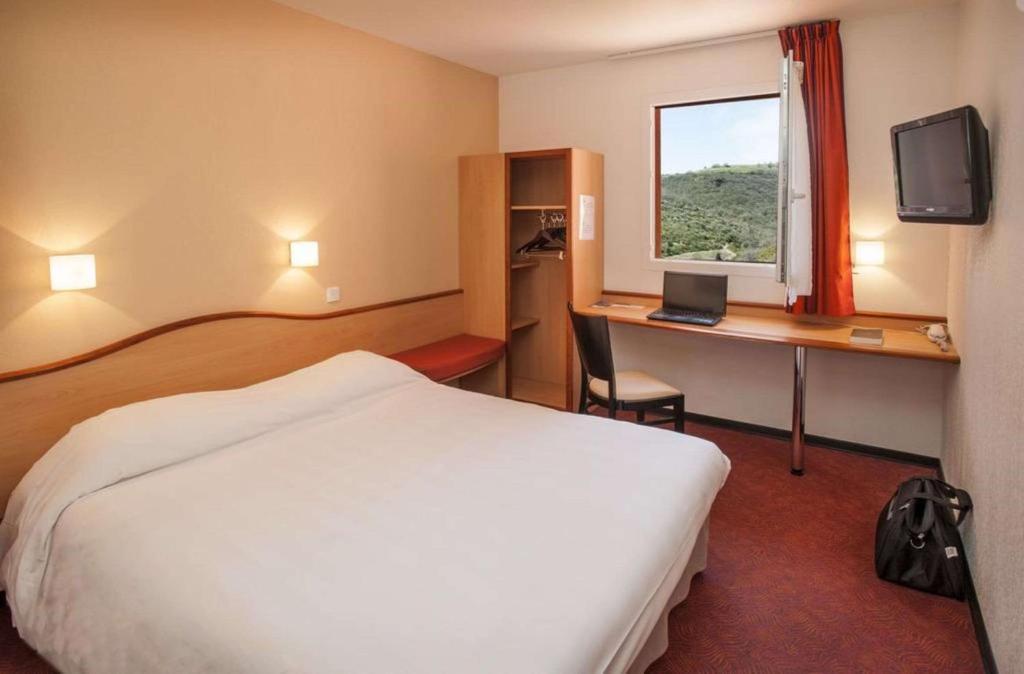 a hotel room with a bed and a desk with a computer at Brit Hotel Confort Montauban in Montauban