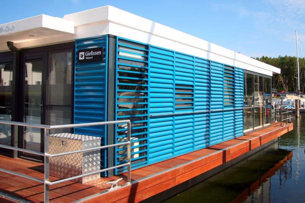 a blue building on a dock next to the water at Hausboot Marama - LP10 in Peenemünde