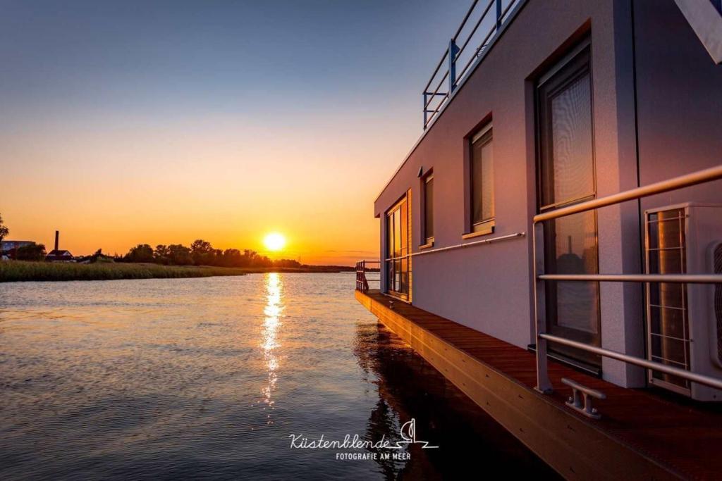 a building on the water with the sunset in the background at Hausboot KranichNest in Ribnitz-Damgarten