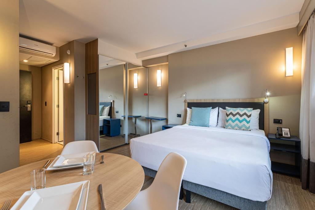 um quarto de hotel com uma cama, uma mesa e cadeiras em Charlie Alphaville em Barueri