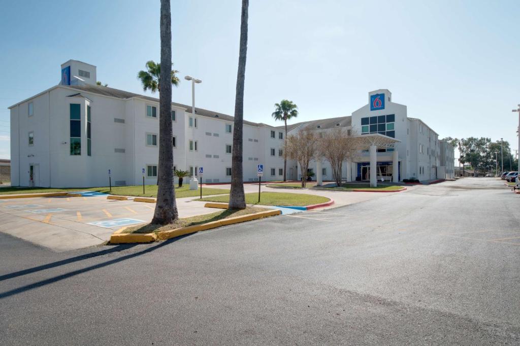2 palmiers dans un parking en face d'un bâtiment dans l'établissement Motel 6-Brownsville, TX, à Brownsville