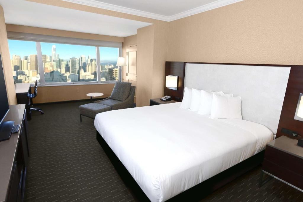 サンフランシスコにあるヒルトン サンフランシスコ ユニオン スクエアの白いベッドと椅子が備わるホテルルームです。
