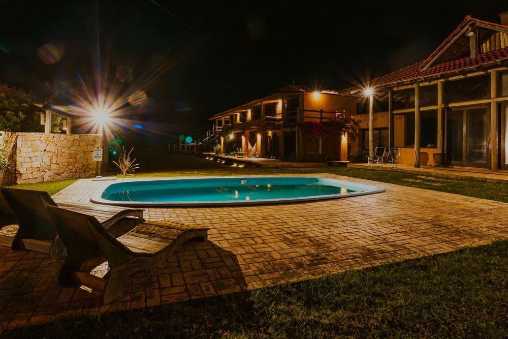 a swimming pool at night with two chairs and a house at Kahuma in Imbituba