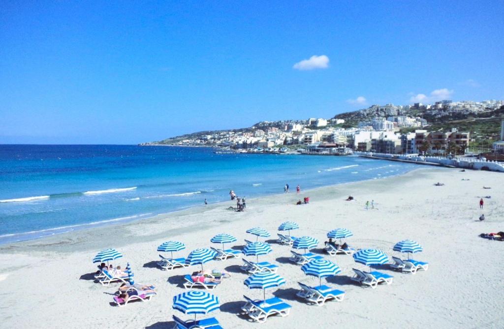 a beach with blue and white umbrellas and the ocean at Seafront Maisonette Ocean Views & Terrace in Mellieħa