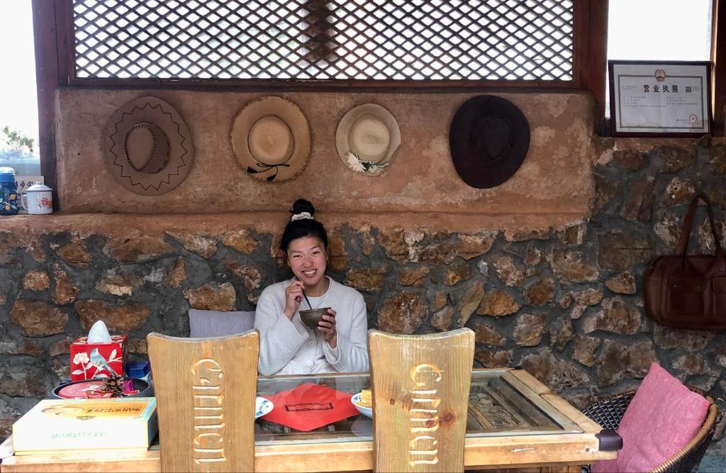 una mujer sentada en una mesa mirando su celular en Lijiang Jayden Lodge臣安山居民宿 - Namaste en Lijiang