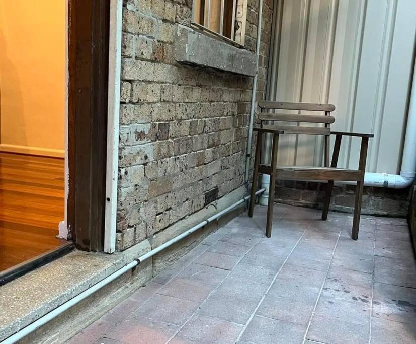 a wooden chair sitting in front of a brick wall at Comfortable Studio+free parking for small car in Sydney