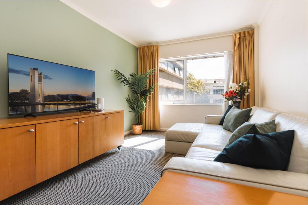 uma sala de estar com um sofá e uma televisão de ecrã plano em Canberra 1-Bed with Pool, Gym, BBQ & Tennis Court em Camberra