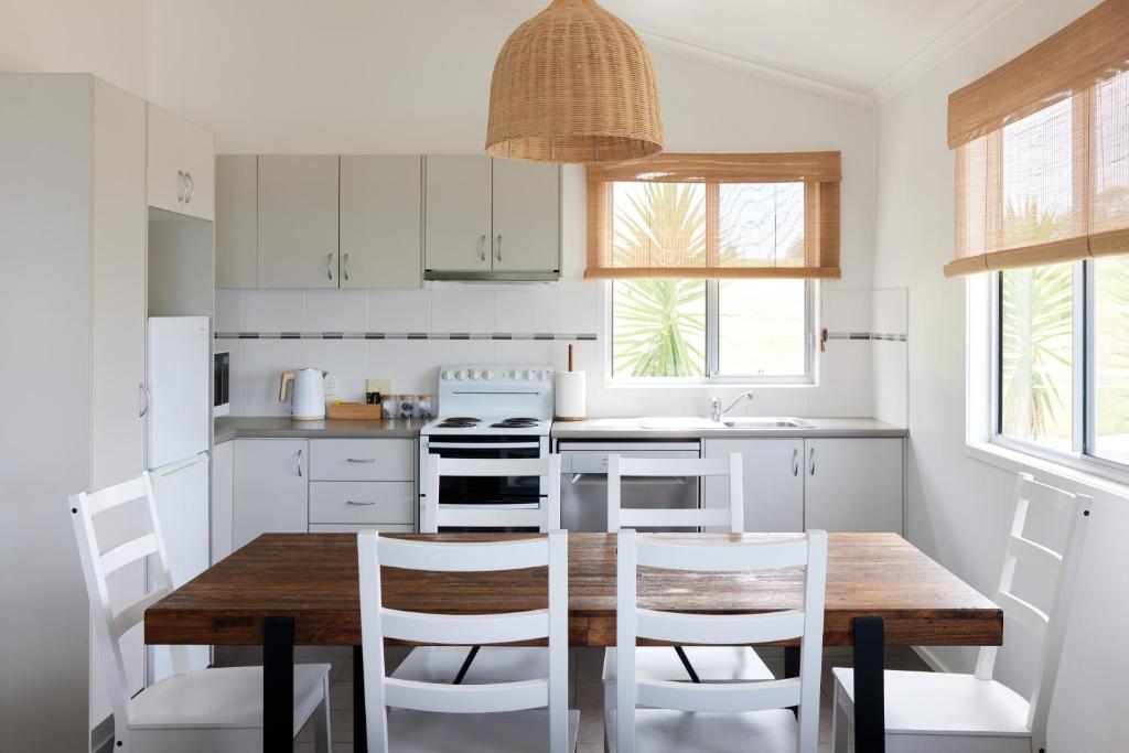a kitchen with a wooden table and white cabinets at Surf Beach Narooma Holiday Park in Narooma