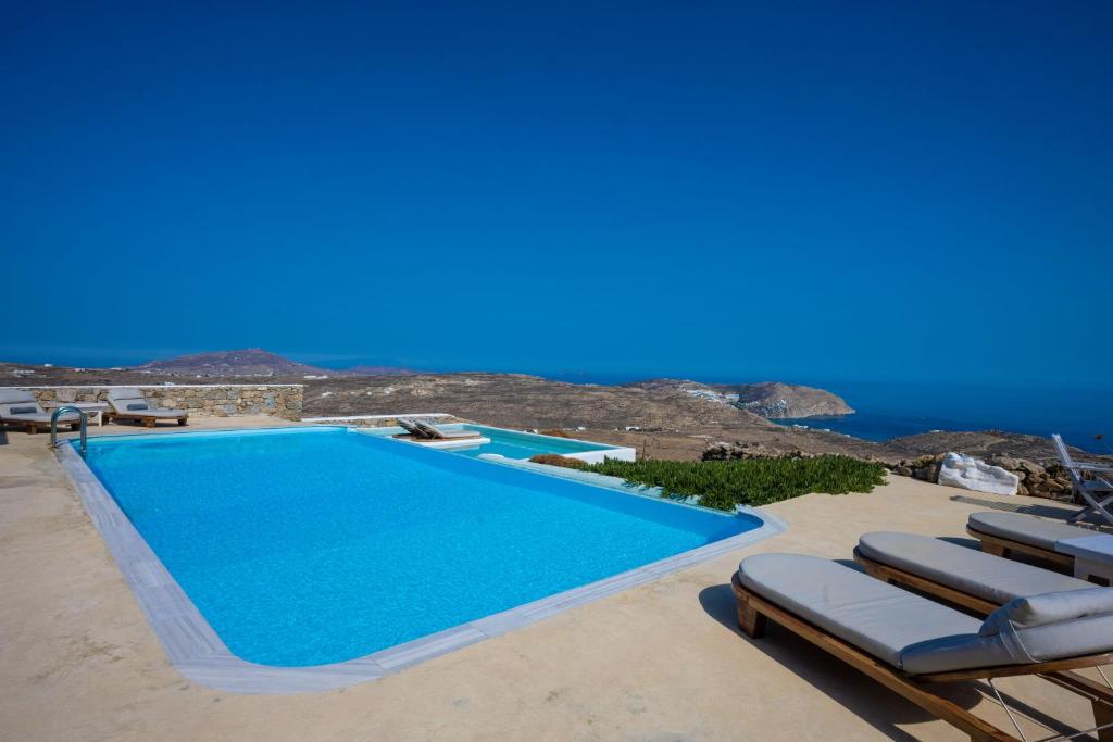 Amallini Suites Mykonos في سوبر بارادايس بيتش: حمام سباحة مع كراسي استرخاء والمحيط