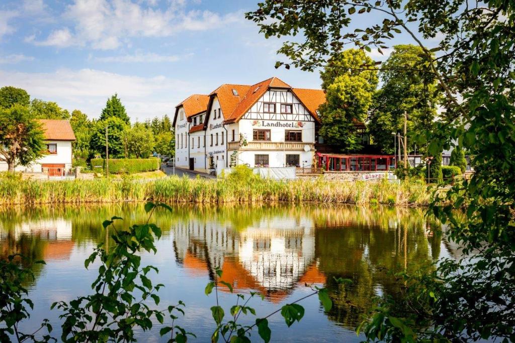 a large white house with a reflection in the water at Landhotel & Reiterhof Schumann in Triptis