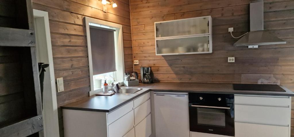 cocina con paredes de madera, armarios blancos y fregadero en Innvik Fjordcamp, en Innvik
