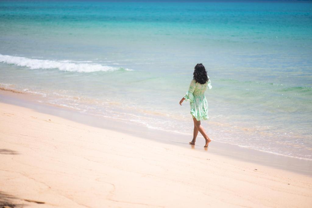 Mantis Soanambo Hotel And Spa في سانت ماري: امرأة تمشي على الشاطئ بالقرب من المحيط