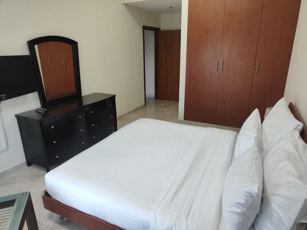 a bedroom with a white bed and a dresser at Al Raya Hotel Apartments in Dubai