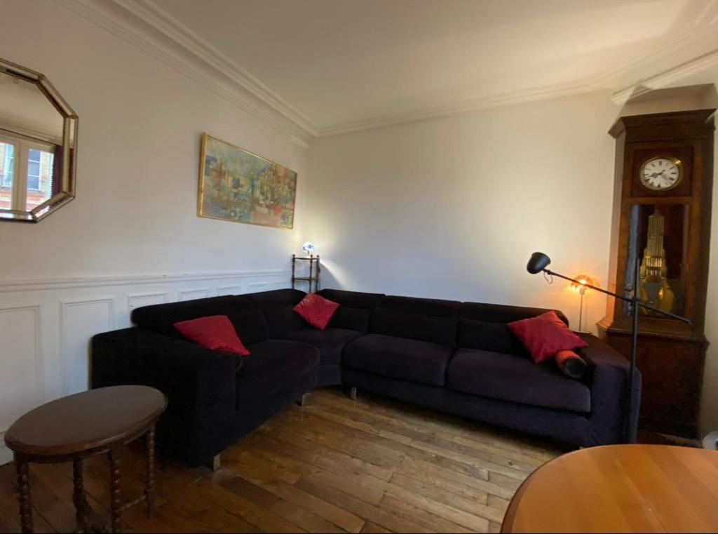 a living room with a black couch and a clock at Jolie appartement 4 pièces in Montreuil