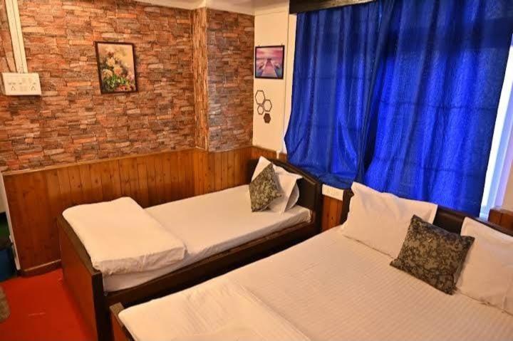 een kamer met 2 bedden en een raam met blauwe gordijnen bij Hotel Birdie's Nest in Darjeeling