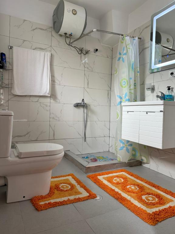La salle de bains est pourvue de toilettes et d'une douche avec des tapis. dans l'établissement Vjosa Guest House, à Memaliaj