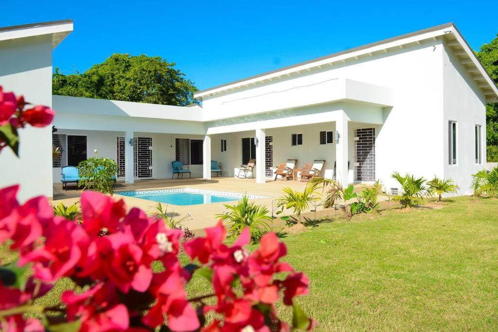 a white house with a pool and red flowers at Retreat2Jamaica in Runaway Bay
