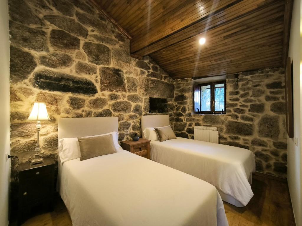 duas camas num quarto com uma parede de pedra em Casa Bodega Sacra em Pereiro de Aguiar