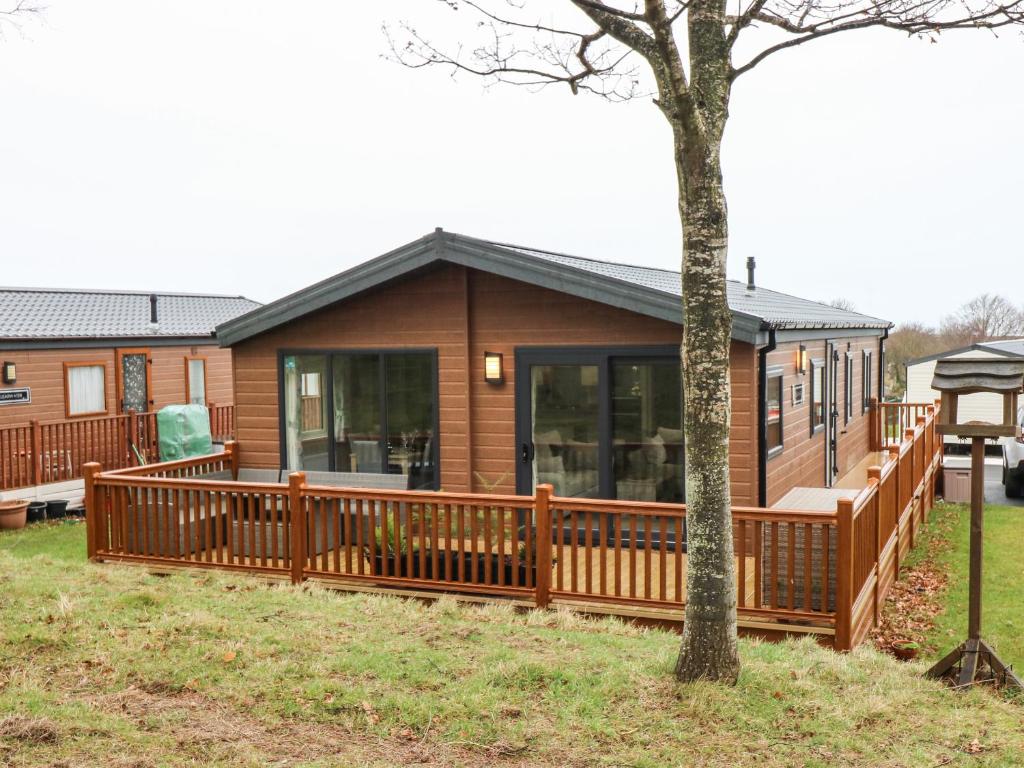 a wooden cabin with a deck and a tree at Woodpecker Lodge in Dunbar