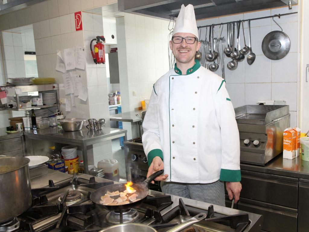 a chef standing in a kitchen cooking food on a pan at Hotel Freiensteinerhof Superior in Sankt Peter-Freienstein