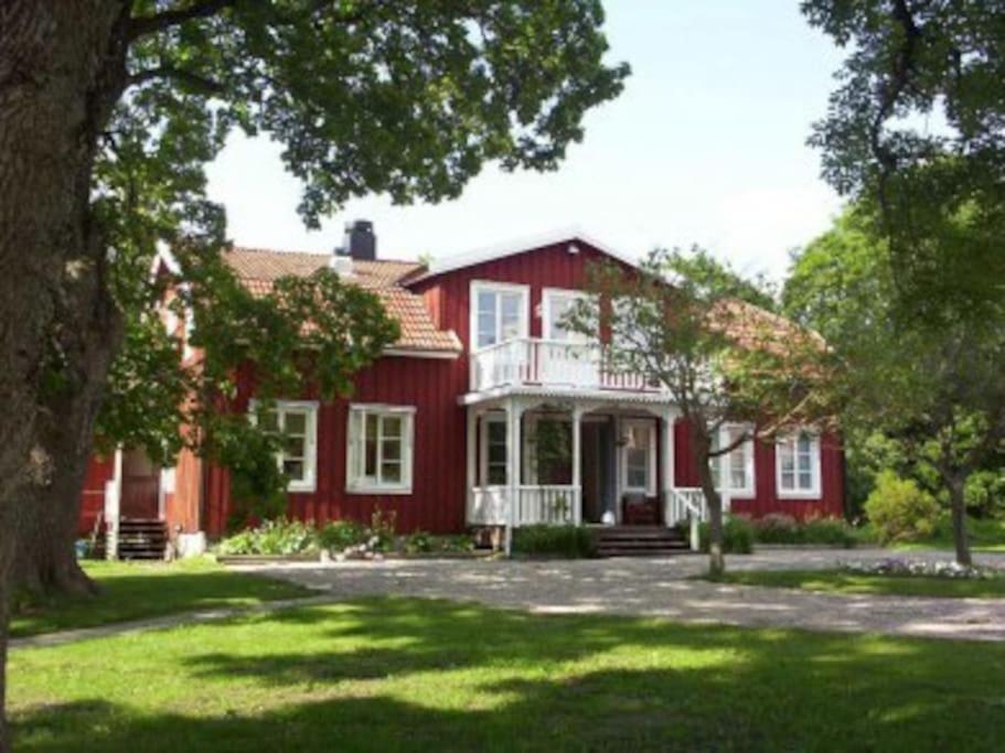 een rood huis met een witte veranda en een boom bij Sörgården - hyr hela gården! (2-35 personer.) in Köping