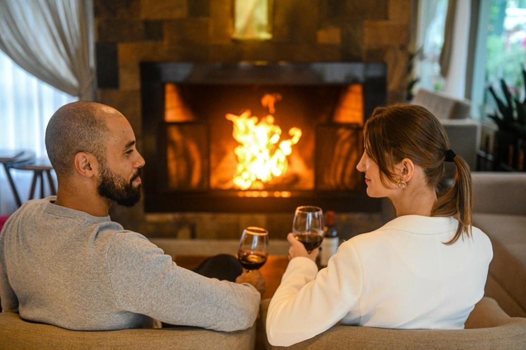 a man and a woman drinking wine in front of a fireplace at Hotel Fioreze Primo in Gramado
