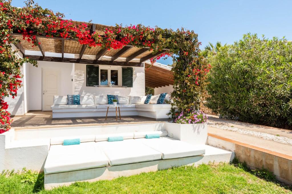 een patio met een pergola met witte meubels en rode bloemen bij Villa Bini Uxuanne by Villa Plus in Binibeca