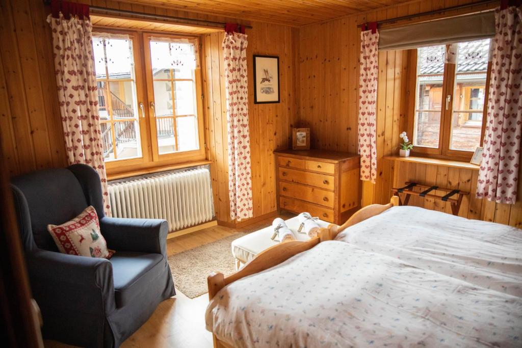 a bedroom with a bed and a chair and windows at Hôtel-Restaurant Le Berger Blancc in Evolène