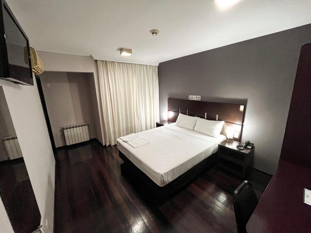 1 dormitorio con cama blanca y suelo de madera en Santa Catarina Plaza Hotel, en Canoinhas