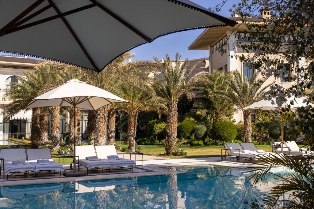 a pool with chairs and umbrellas next to a building at Palais Ronsard Relais & Chateaux in Marrakech