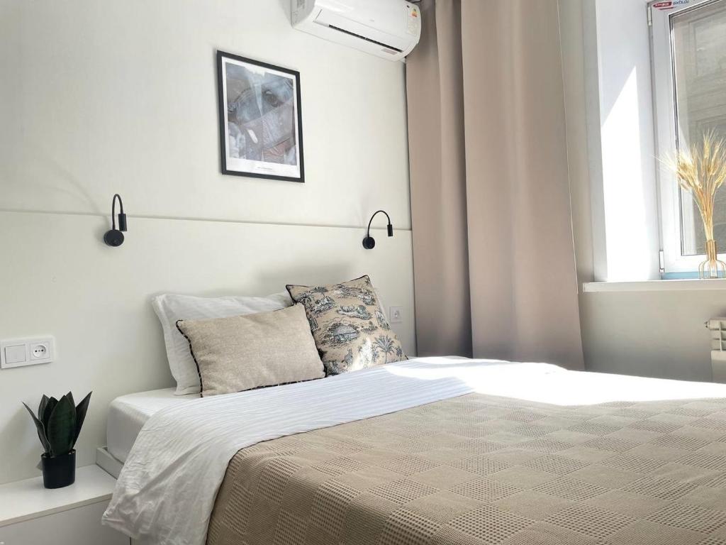 a white bedroom with a bed with a window at Seven City Apartments in Semey
