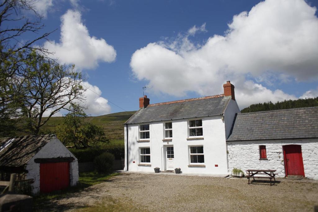 ein weißes Haus mit roten Türen und einer Bank in der Unterkunft Mynydd Crwn Bach Clynderwen in Clynderwen