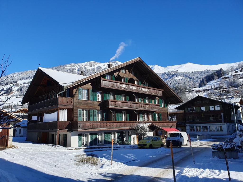un grand bâtiment dans la neige avec une camionnette devant dans l'établissement Hotel Garni Alpenruh, à Lenk im Simmental