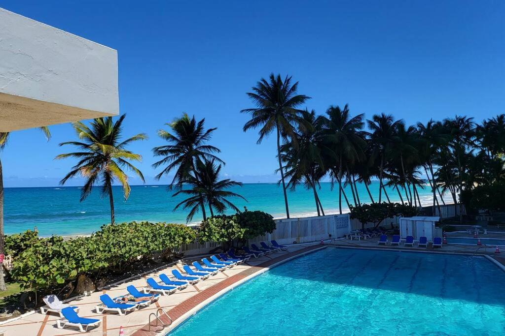 a swimming pool with chairs and palm trees and the ocean at Ocean View 1 Bedroom Cabana in Condado! in San Juan