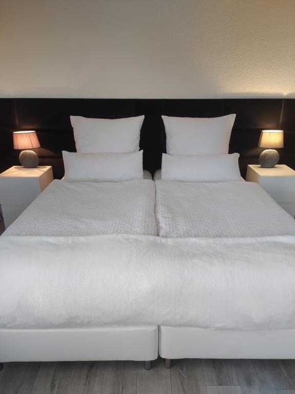 Una cama con sábanas blancas y almohadas en un dormitorio en Haus am Waldrand en Bad Hersfeld