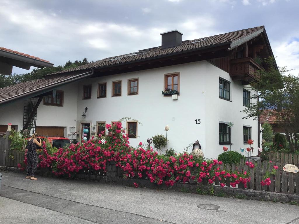 een vrouw die voor een wit huis met bloemen staat bij Ferienwohnung am Moosbach in Anger