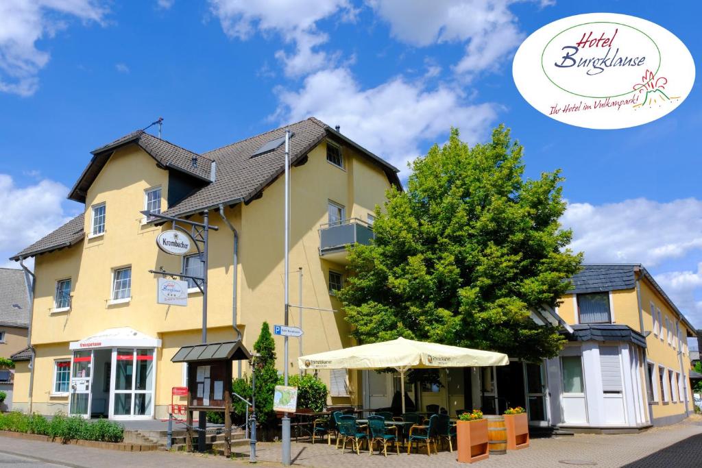 ein gelbes Gebäude mit einem Regenschirm und einem Baum in der Unterkunft Hotel Burgklause in Nickenich