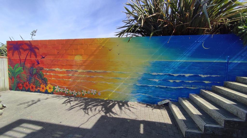 a rainbow mural on a wall next to a staircase at Coastal Condo in Waitarere