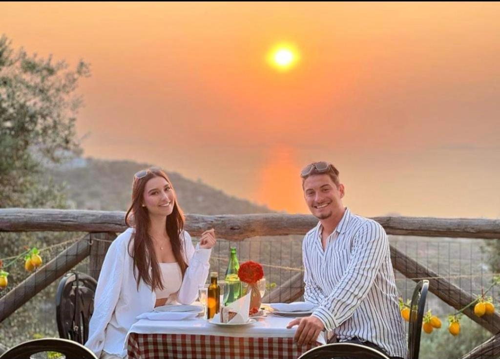 Ein Mann und eine Frau sitzen an einem Tisch vor dem Sonnenuntergang. in der Unterkunft Agriturismo Le Grottelle in SantʼAgata sui Due Golfi