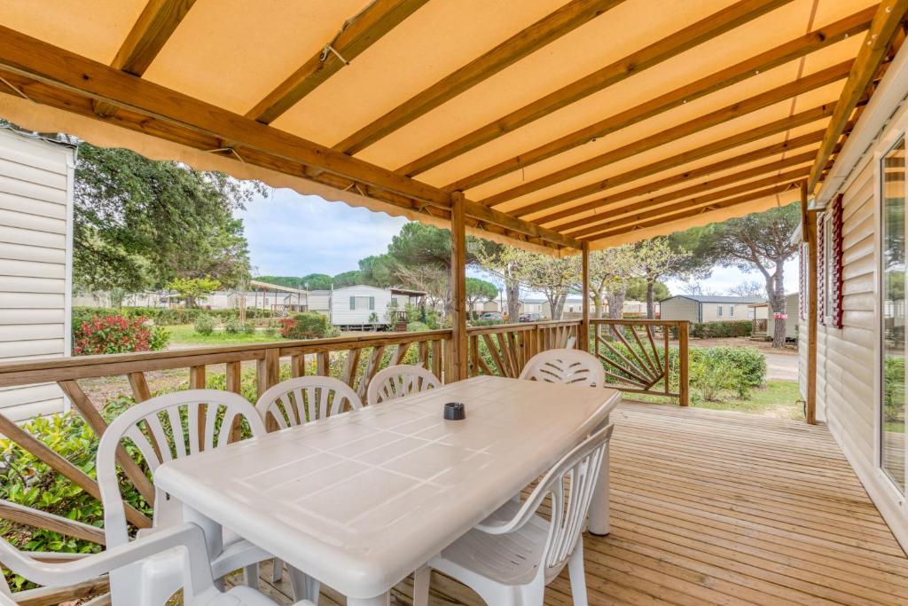 une terrasse en bois avec une table et des chaises blanches dans l'établissement Mobilhome 530 - 8 personnes, à Lattes