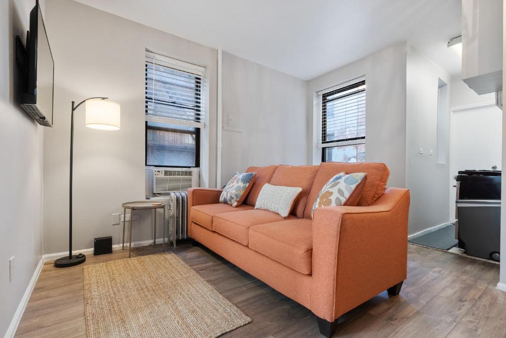 an orange couch in a living room with two windows at Centrally located Manhattan apartments ,Times Square/Hell’s kitchen in New York